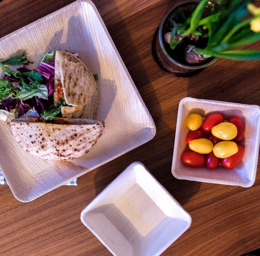 Palm leaf plates Israel — square areca palm leaf plate with stuffed pita bread halves and mixed salad greens, paired with cherry tomato side bowl, Mediterranean cafe presentation for Israeli wholesale distributors, kosher-certified caterers and hospitality buyers