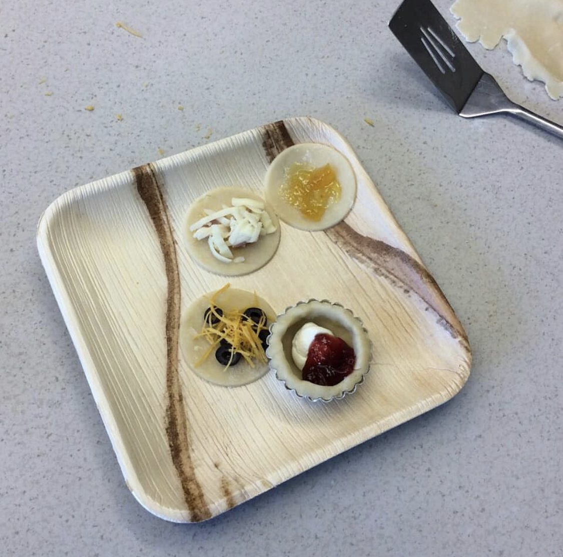 Areca palm leaf plates and bowls in lifestyle picnic service — salad, fresh fruit platter, and wrap rolls plated for outdoor dining, illustrating Ecodyne wholesale tableware in real HoReCa use for Finnish distributors and event caterers
